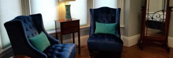 two dark blue chairs set in bay window, with lamp inbetween and mirror to the side