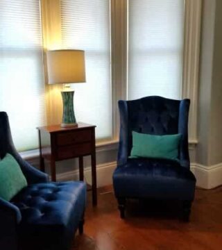 two dark blue chairs set in bay window, with lamp inbetween and mirror to the side