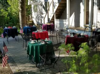 back patio area with tables with multicolored tablecloths, set for a meal